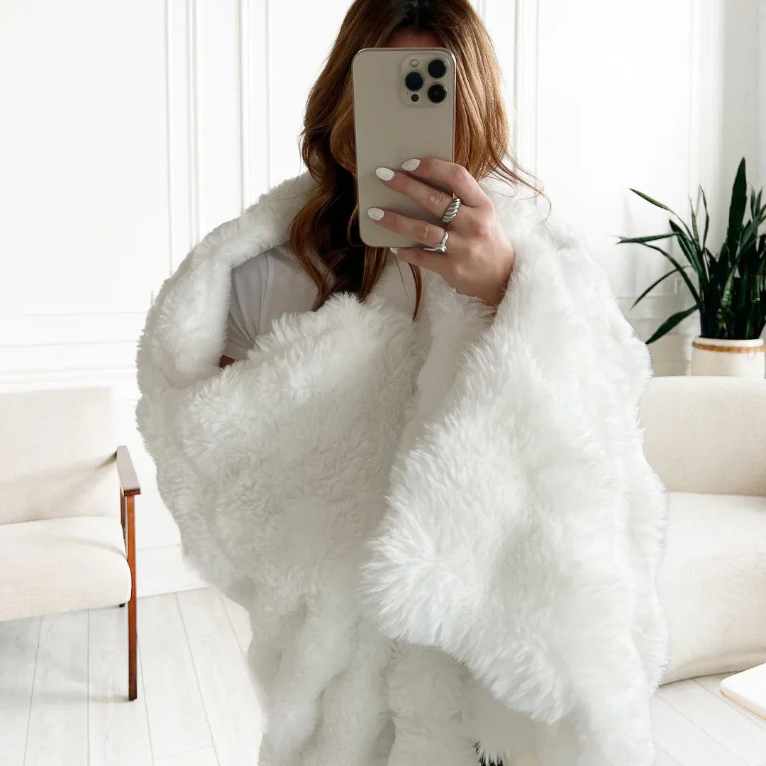 Woman wrapped in a fluffy white blanket, taking a selfie.