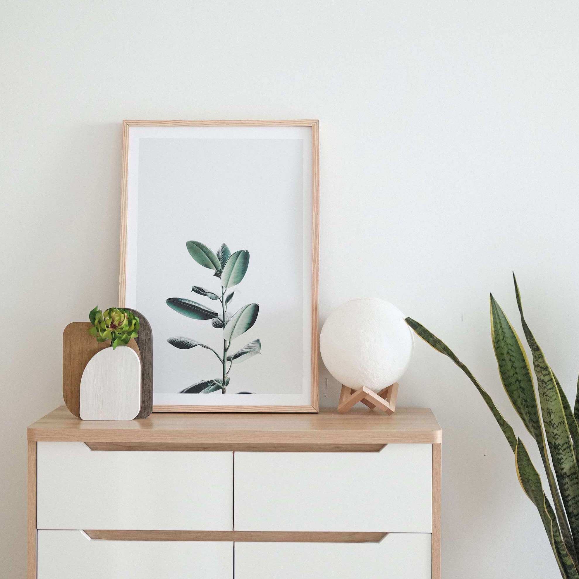 Wooden dresser with decor and a framed plant print.